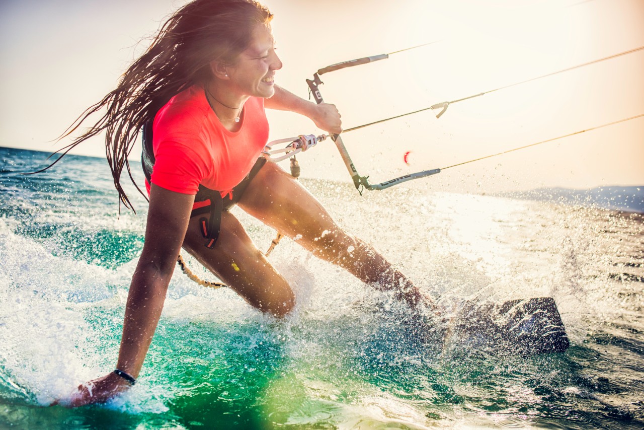 Smiling young woman kiteboarding on the sea holding the strap and tracing her hand in the water.